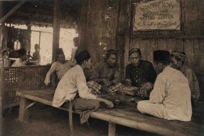 Ilustrasi Sejumlah pria duduk melingkar di warung kopi bambu di Tjiong Hwa, Serang-Banten, dengan suasana percakapan serius dan papan nama warung di dinding; ilustrasi bernuansa arsip kolonial yang menampilkan ruang diskusi rakyat kecil di awal abad ke-20. (ardiholmes.id)