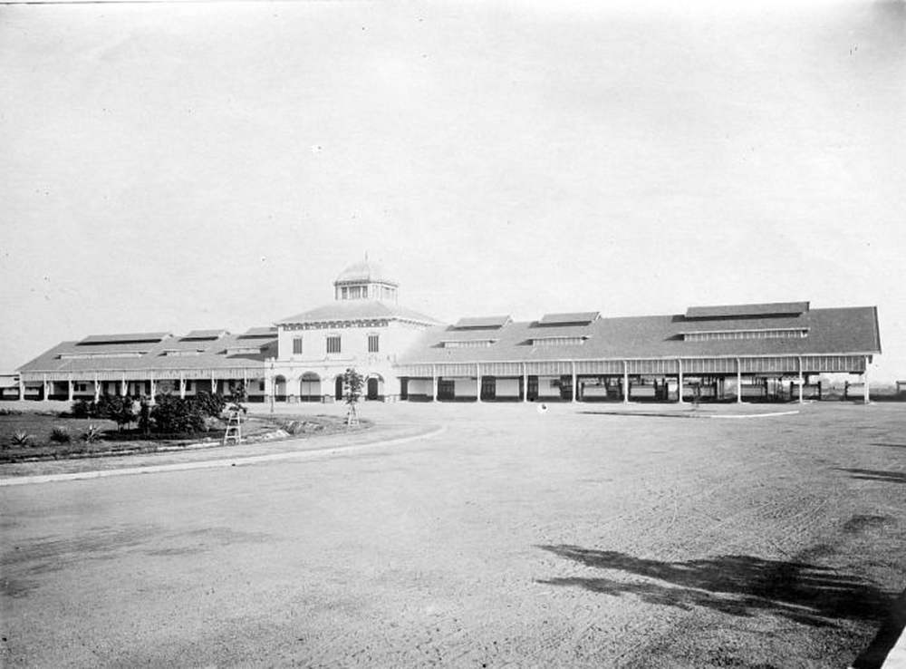Foto hitam putih sebuah stasiun kereta api kolonial di Semarang, Jawa Tengah. Bangunan stasiun bergaya Eropa dengan atap lebar dan deretan tiang penyangga peron. Beberapa orang berdiri di sepanjang peron. Rel memanjang ke arah kanan bingkai. Gambar diambil antara 1910 dan 1920 oleh fotografer tak dikenal, koleksi Tropenmuseum.