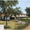 ​Foto bangunan rumah gadai pemerintah kolonial Hindia Belanda (pandhuis) yang terletak di belakang rumah dinas Asisten Residen di Yogyakarta sekitar tahun 1910, menampilkan arsitektur bangunan beratap genting dengan halaman rumput yang luas (ardiholmes.id)