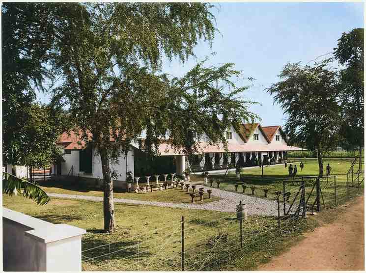 ​Foto bangunan rumah gadai pemerintah kolonial Hindia Belanda (pandhuis) yang terletak di belakang rumah dinas Asisten Residen di Yogyakarta sekitar tahun 1910, menampilkan arsitektur bangunan beratap genting dengan halaman rumput yang luas (ardiholmes.id)