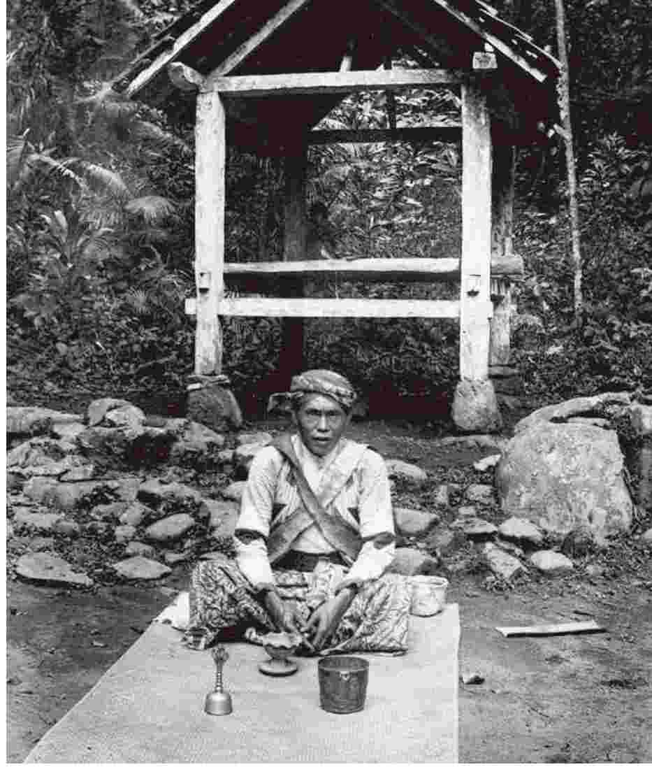 Seorang dukun dari Kandangan, dekat Lumajang, Jawa Timur, duduk di atas tikar dengan lesung dan berbagai perlengkapan pengobatan tradisional di depannya. (ardiholmes.id)